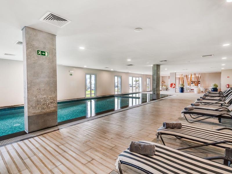 Indoor area with a long swimming pool, lounge chairs, and large windows providing ample daylight.