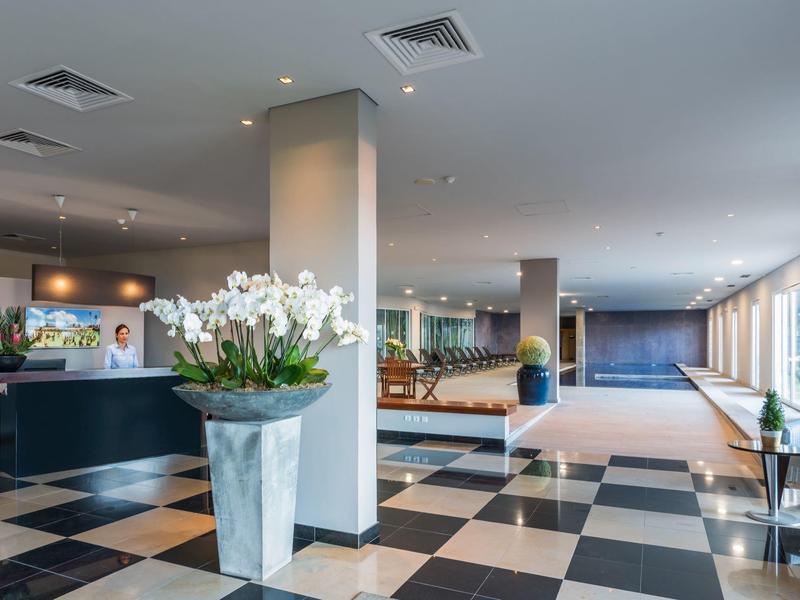 Bright hotel lobby with reception, orchids, and checkered black-and-white flooring.