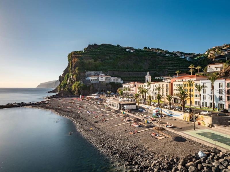 Coastal town with beach, cliffs, and buildings at sunset.