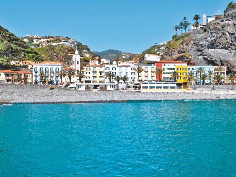 Colorful buildings along a rocky coast with clear blue water in the foreground.