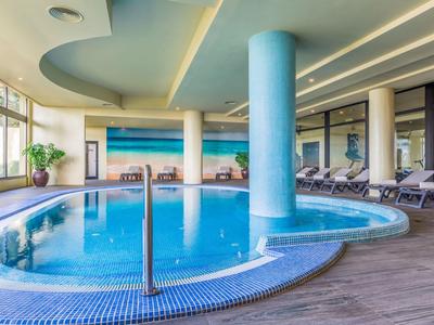 Innen beheizter Pool mit runder Form, blauen Fliesen und Liegestühlen im hellen Wellnessbereich.