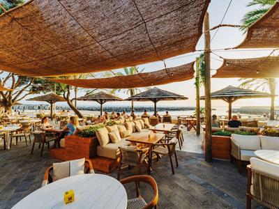 Outdoor-Restaurant mit Holzmöbeln und Sonnensegeln mit Meerblick bei Sonnenuntergang.
