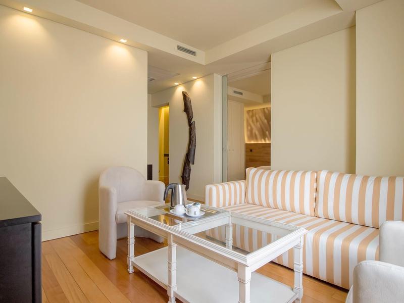 Heller Wohnraum mit gestreiftem Sofa, weißen Sesseln, Glas-Couchtisch und Flachbildfernseher.