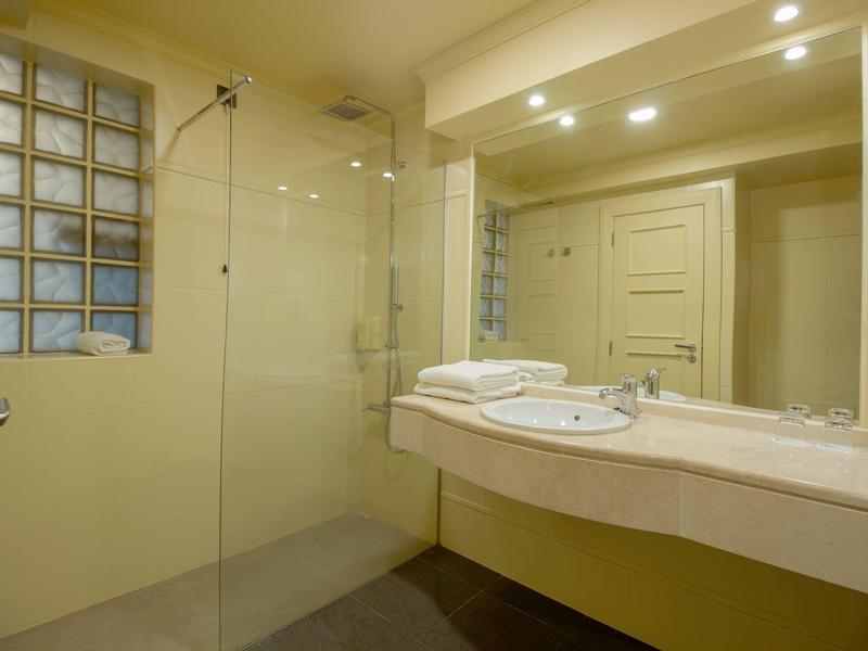 Modernes Badezimmer mit Glasdusche, großem Spiegel, weißen Handtüchern und hellem Waschbecken.