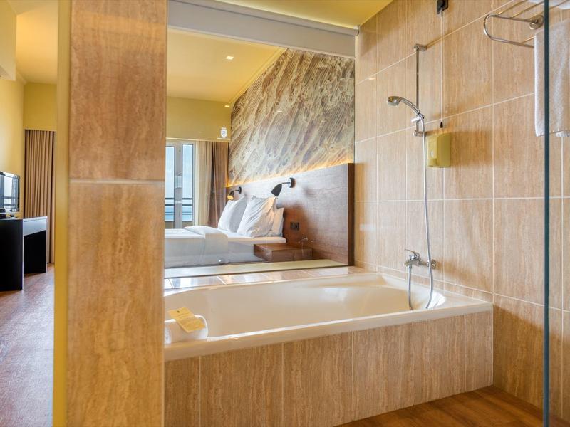 Modernes Badezimmer mit großer Badewanne, beiger Fliesenwand und Blick ins Schlafzimmer.
