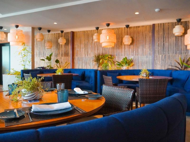 Modernes Restaurant mit blauen Sitzbänken, Holztischen, grünen Pflanzen und warmem Licht.