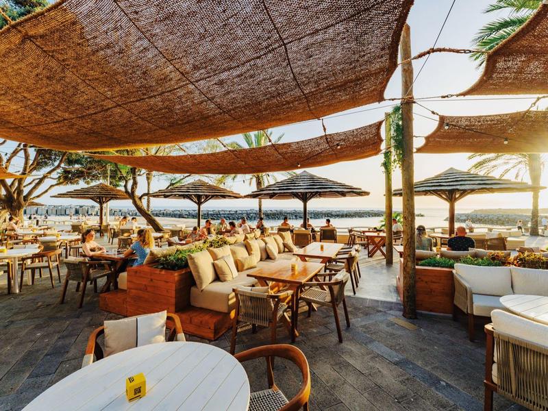 Outdoor-Restaurant mit Holzmöbeln und Sonnensegeln mit Meerblick bei Sonnenuntergang.