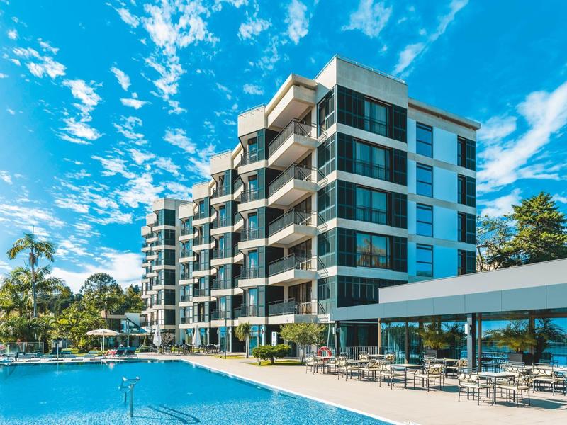 Moderní hotelový komplex s velkým venkovním bazénem a sluneční terasou za jasné oblohy.