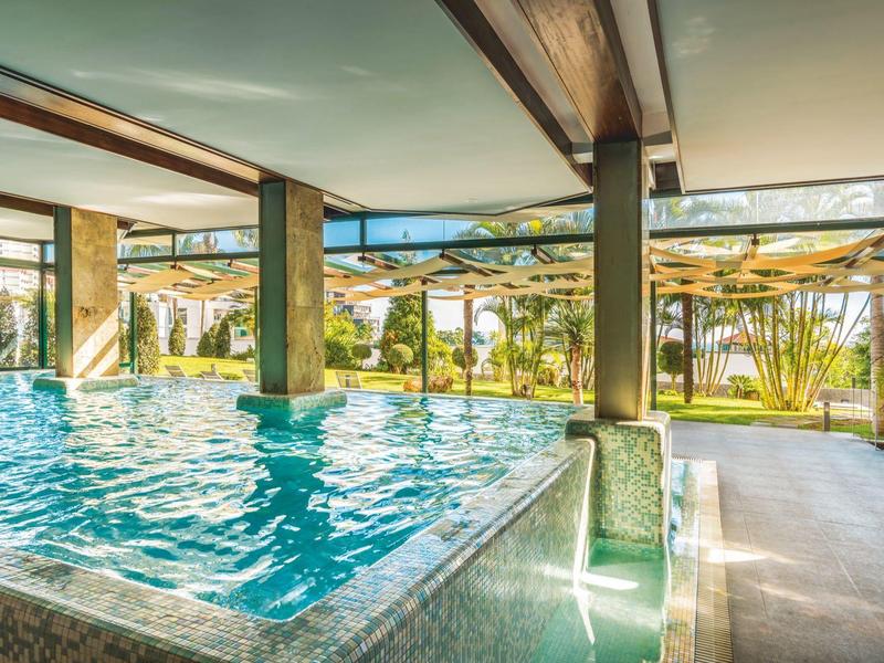 Světle krytý bazén s velkými okny s výhledem na zahradu s slunečníky.