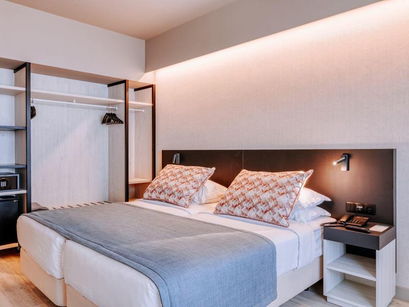 Moderní hotelový pokoj s manželskou postelí, otevřenou skříní a měkkým osvětlením.