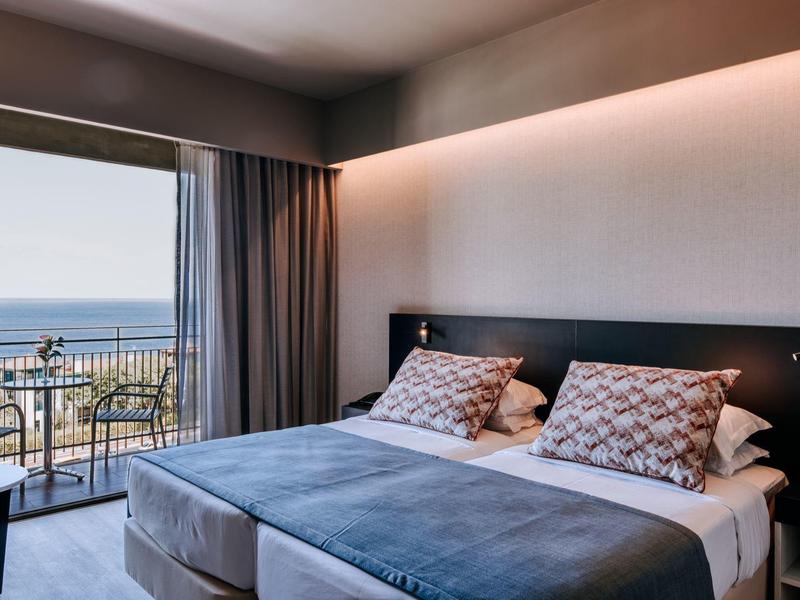Moderní hotelový pokoj s manželskou postelí a balkónem s výhledem na moře.