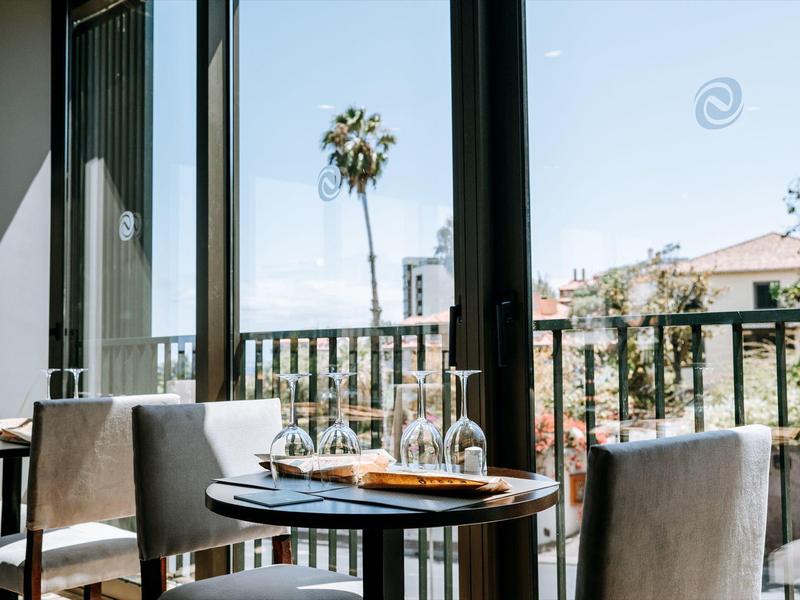 Moderní jídelní prostor s prostřeným stolem a výhledem na palmu a budovy.