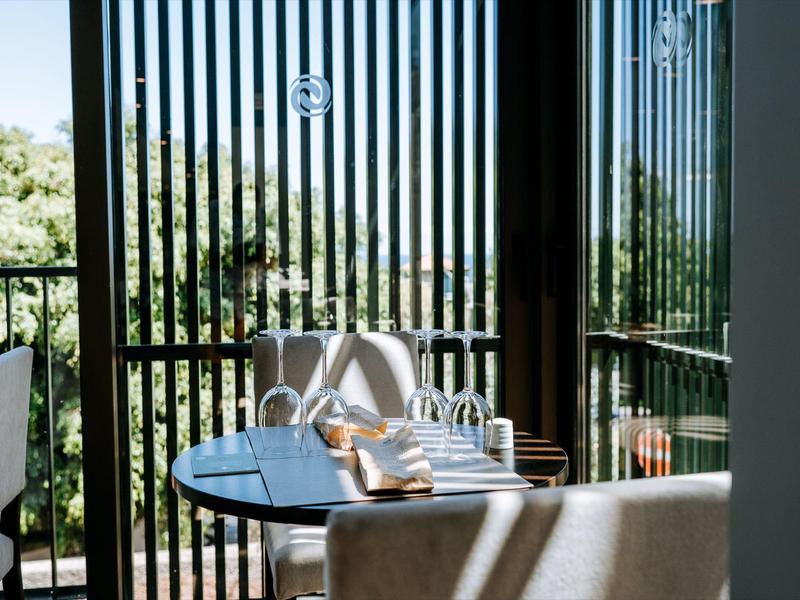 Moderní venkovní prostor se stolem, židlemi a skleněným zábradlím obklopený zelení.