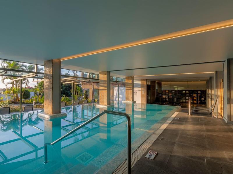 Moderní krytý bazén se skleněnými stěnami a přímým vstupem na venkovní terasu v hotelu.