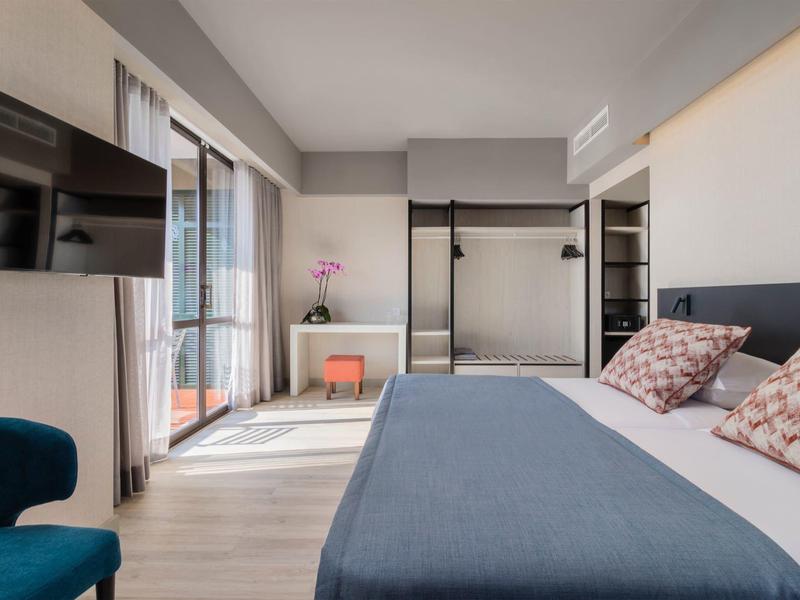 Moderní hotelový pokoj s velkou postelí, balkónem a otevřenou skříní.