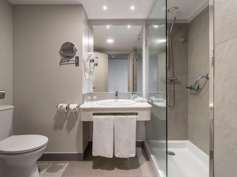 Moderní hotelová koupelna se sprchou, toaletou a umyvadlem s ručníky.