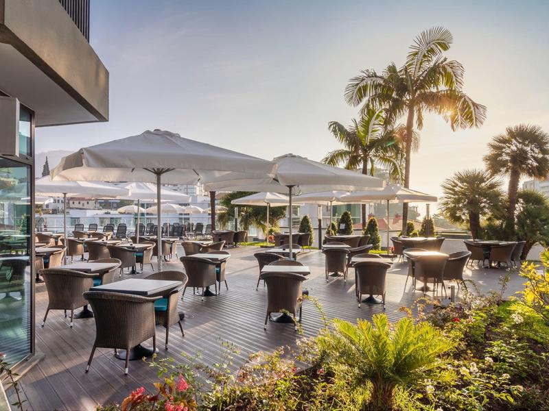 Terasa s stoly, židlemi, slunečníky a palmami za západu slunce