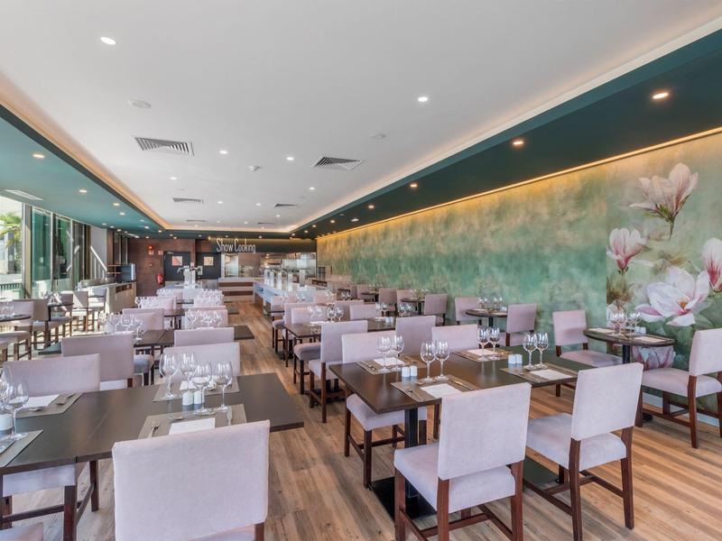 Moderní hotelová restaurace s prostřenými stoly a květinovou nástěnnou dekorací.