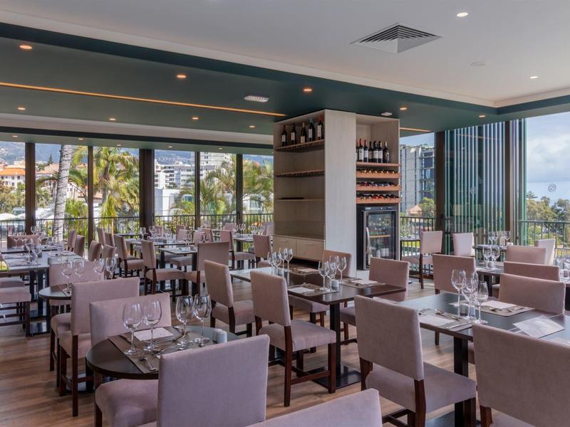 Moderní restaurace s prostřenými stolky a velkými okny s výhledem na palmy