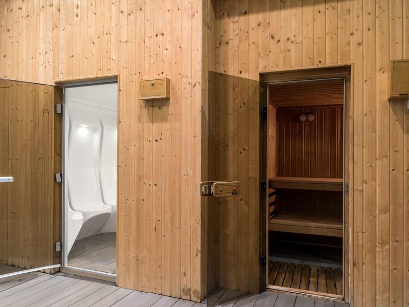 Dve dřevěné dveře vedou do sauny a moderní sprchové části v relaxačním prostoru.