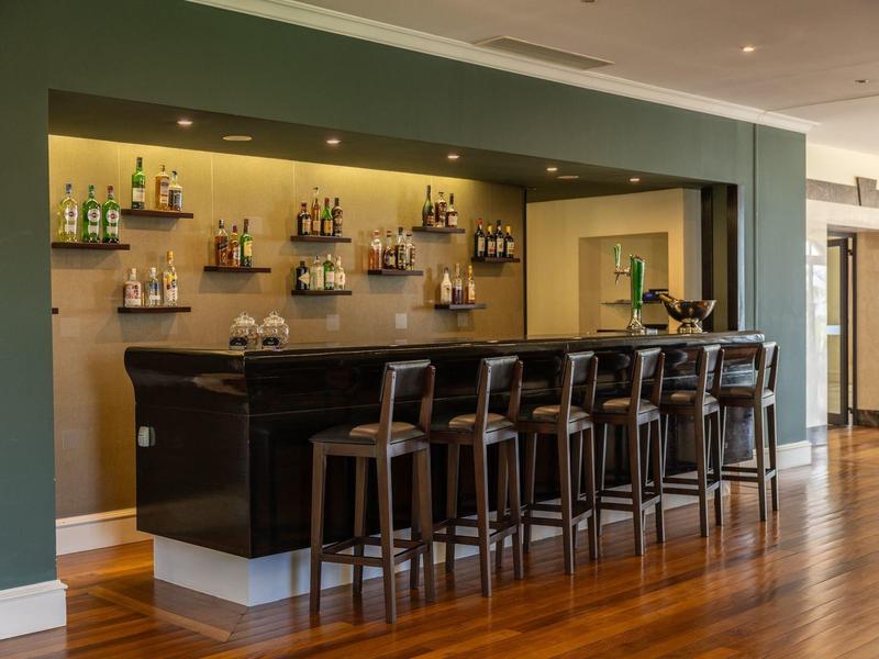 Moderní hotelový bar s sedmi dřevěnými židlemi a vestavěným regálem na lihoviny.