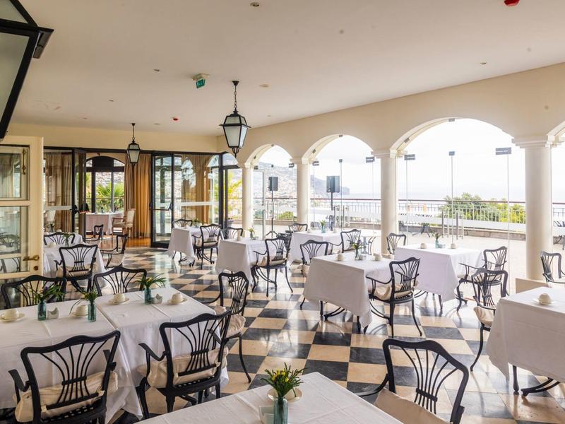 Světle osvětlený elegantní restaurace s bílými stoly a kovovými židlemi u velkých oblouků.