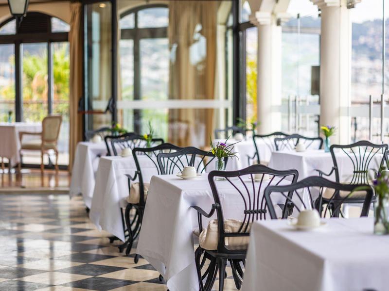 Elegantní restaurace s bílými ubrusy a výhledem na město za denního světla.