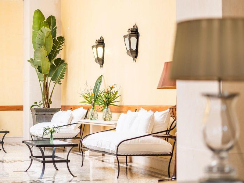Světlý salon s bílými pohovkami, rostlinami a nástěnnými lampami pro hotelové hosty.