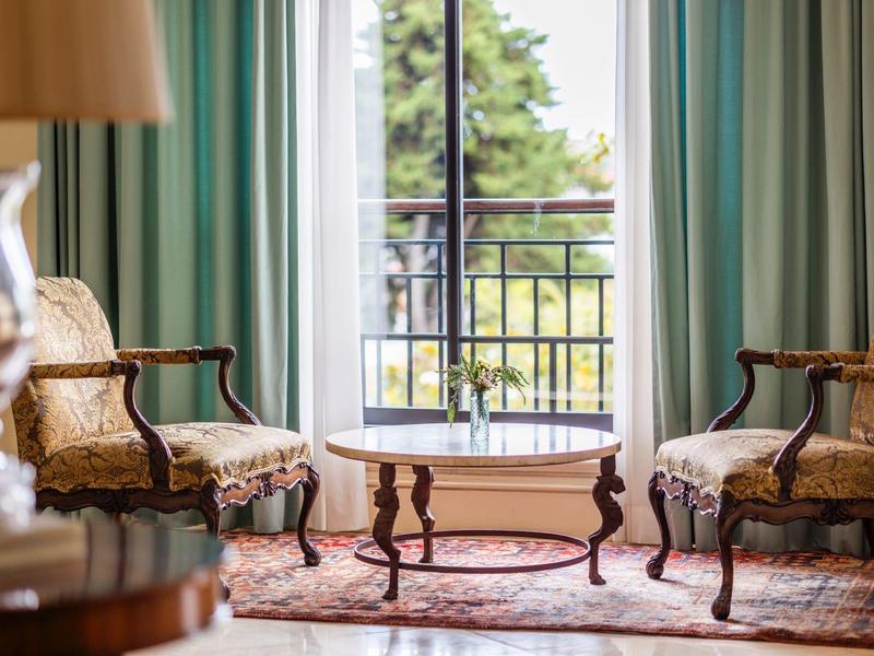 Elegantní obývací pokoj se dvěma starožitnými křesly, dřevěným stolem a výhledem na balkon a zahradu.