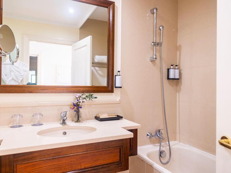 Světelná koupelna s dřevěným zrcadlem, umyvadlem, vanou a sprchou.