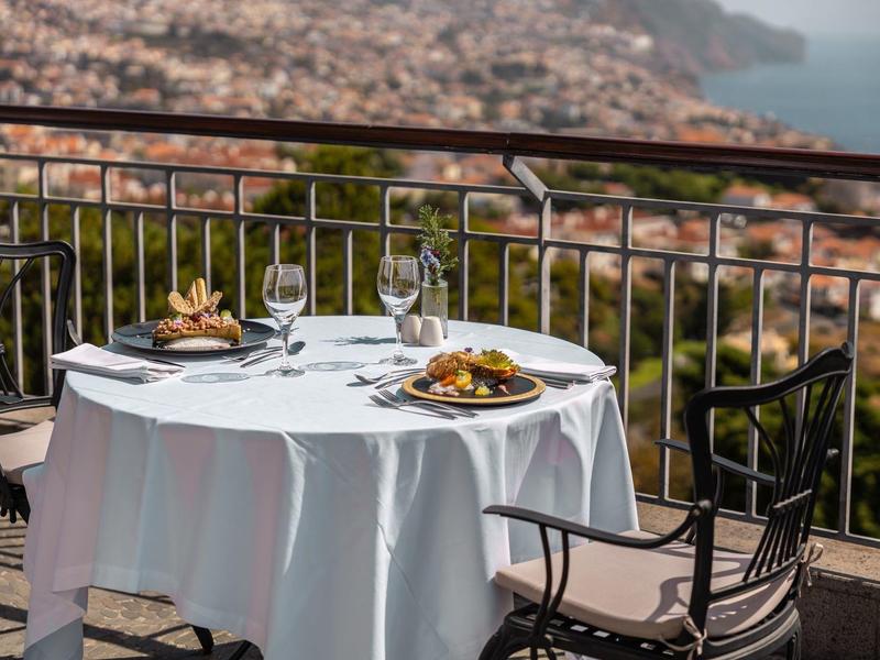 Stůl s pokrmy a sklenicemi na terase s výhledem na město a moře.