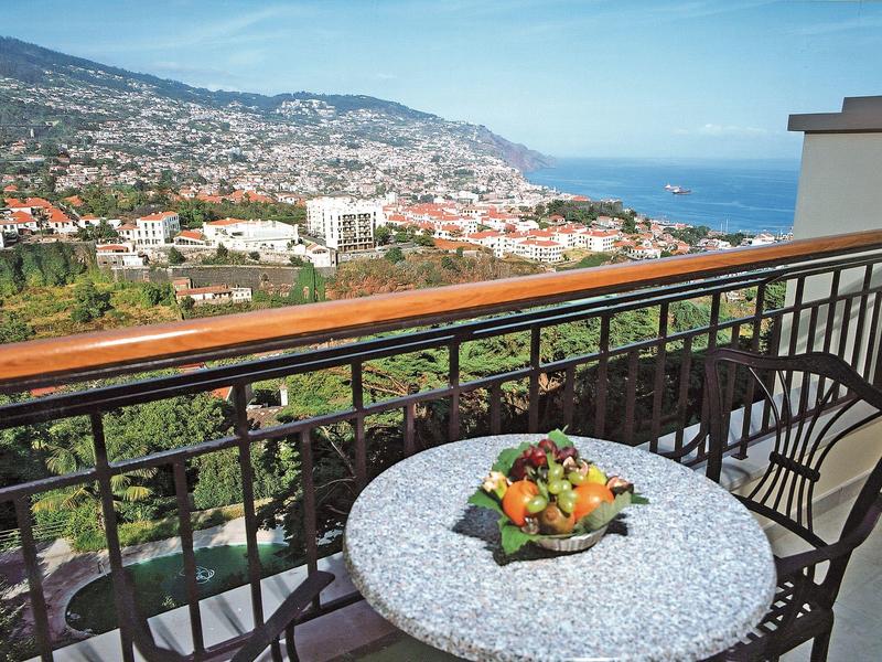 Balkon se stolem a ovocnou miskou, výhled na kopce, město a moře v pozadí.