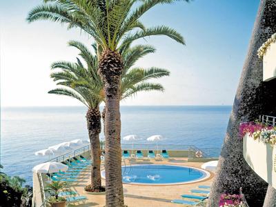 Poolbereich mit Palmen und Meerblick bei klarem Himmel