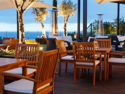 Außenrestaurant mit Holztischen und Stühlen auf einer Terrasse mit Meerblick bei Sonnenuntergang.