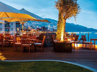 Außenterrasse mit Holztischen und Stühlen, Blick auf Meer und Berge bei Dämmerung