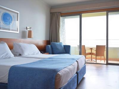Modern eingerichtetes Hotelzimmer mit zwei Betten und Zugang zu einem Balkon mit Stühlen.