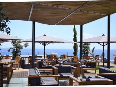 Terrasse eines Hotels mit Sitzbereichen aus Holz und Blick aufs Meer, bedeckt von Sonnenschirmen.