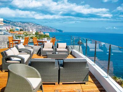 Hotelterrasse mit Sesseln und Tischen mit Meerblick bei klarem Himmel