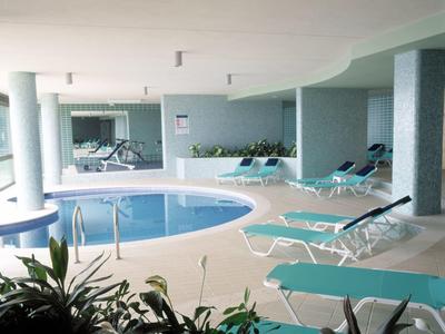 Innenbereich mit rundem Schwimmbad, Liegestühlen und Pflanzen in einem Hotel.