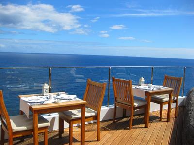 Terrasse eines Hotels mit Holztischen und -stühlen mit Blick auf das Meer unter blauem Himmel