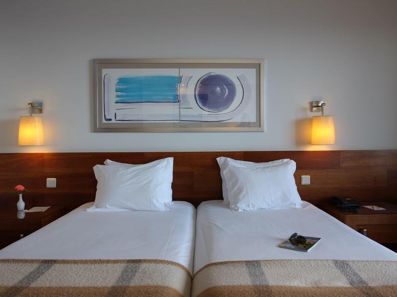 Zwei Einzelbetten mit weißen Kissen und Decken, zwei Wandlampen und abstraktes Bild über dem Kopfteil.