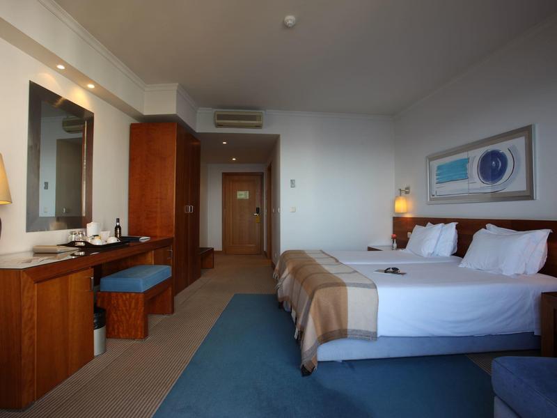 Modernes Hotelzimmer mit Doppelbett, Schreibtisch, Spiegel und indirekter Beleuchtung.