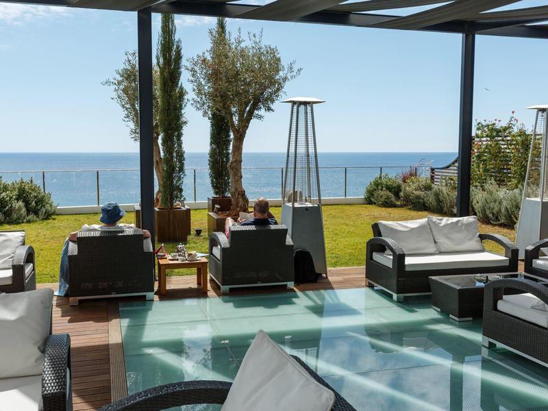 Lounge-Bereich mit Sitzmöbeln und Blick auf das Meer bei sonnigem Wetter.