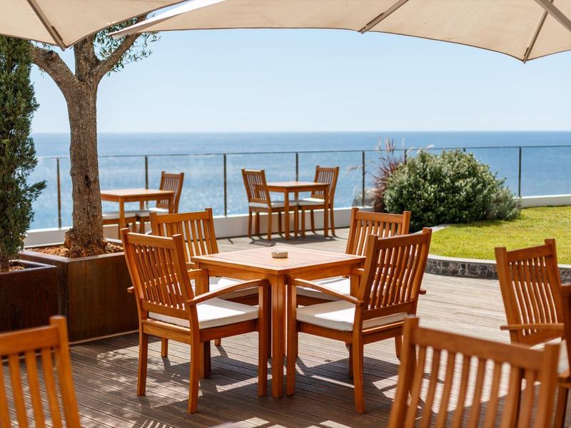 Terrasse mit Holzstühlen und Tischen mit Blick aufs Meer bei klarem Himmel