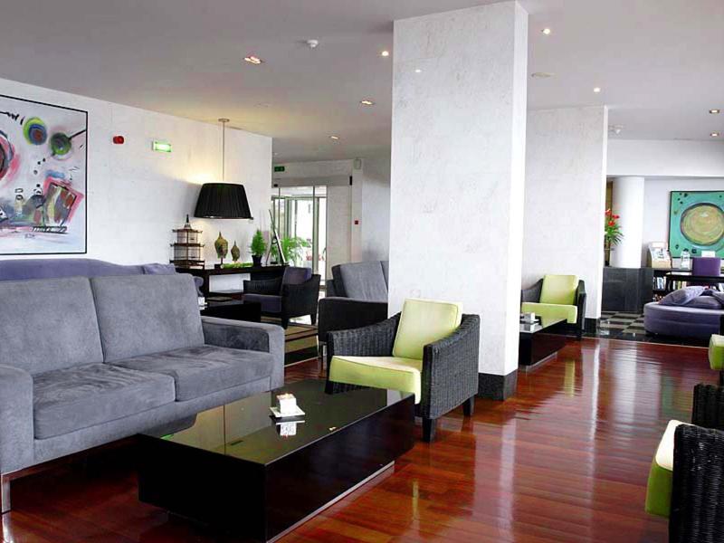 Moderne Lounge mit grauem Sofa, grünen Sesseln, schwarzen Tischen und bunten Wandbildern.
