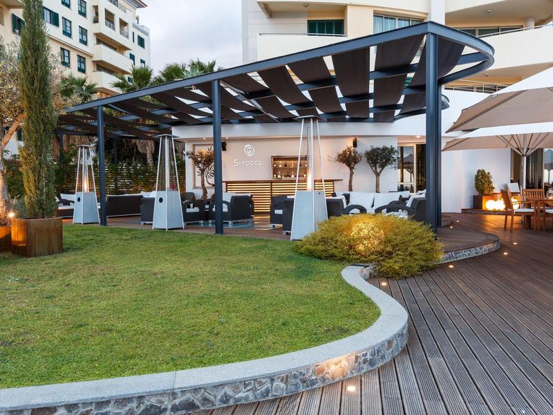 Moderne überdachte Lounge-Sitzbereiche neben einem Hotel mit Holzterrasse und grünem Rasen