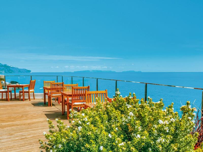 Holzterrasse mit Tischen und Stühlen am Meer mit Blumenim Vordergrund