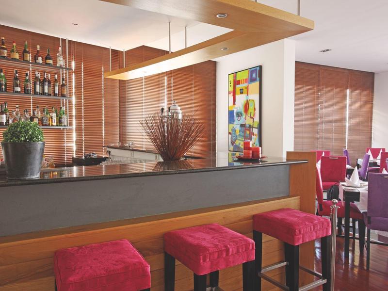 Moderne Hotellounge mit Holzpanelen, Barhockern in Rot und einer Bar im Hintergrund.