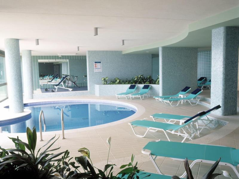 Innenbereich mit rundem Schwimmbad, Liegestühlen und Pflanzen in einem Hotel.