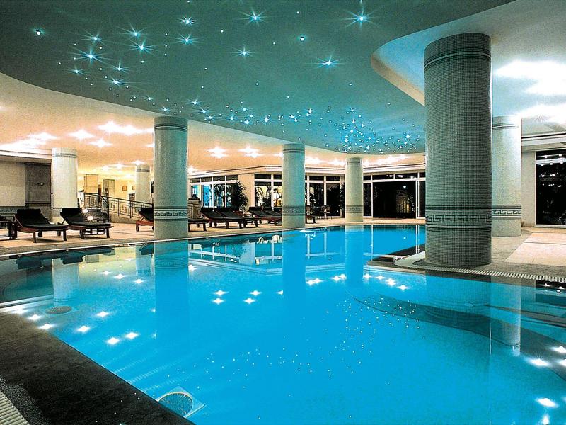 Piscina coperta con acqua illuminata di blu e lettini in un interno moderno di hotel